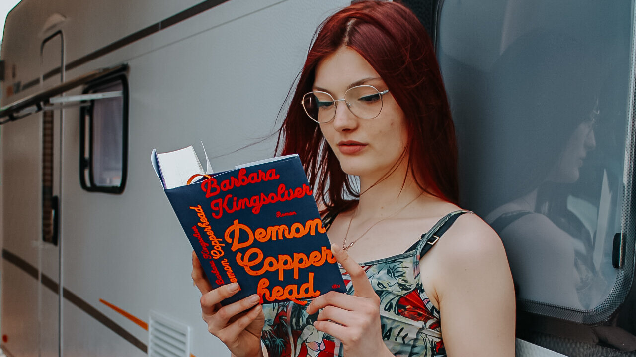 Demon Copperhead Roman von Barabara Kingsolver wird von einem rothaarigen Mädchen gelesen